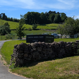 Chevin Green Farm sign on a stone wall with a scenic background of green fields and trees.