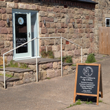 Three steps up lead to Godfrey's Ear front door, with a logo and a Fusion Mineral Paint sign. The A-board stands in front of the steps.